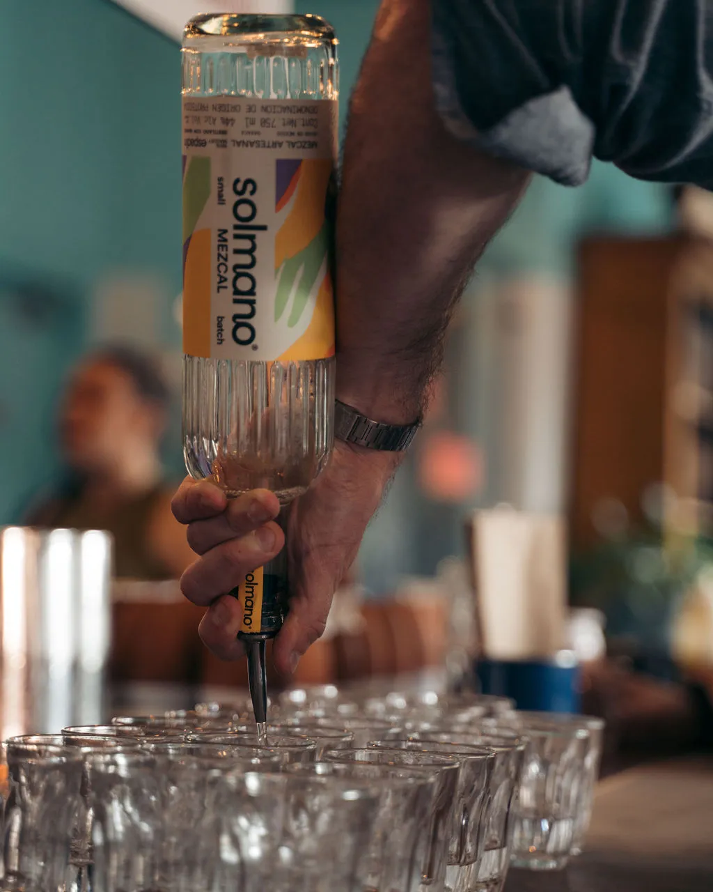 A bottle of Solmano mezcal upended over a row of tasting glasses