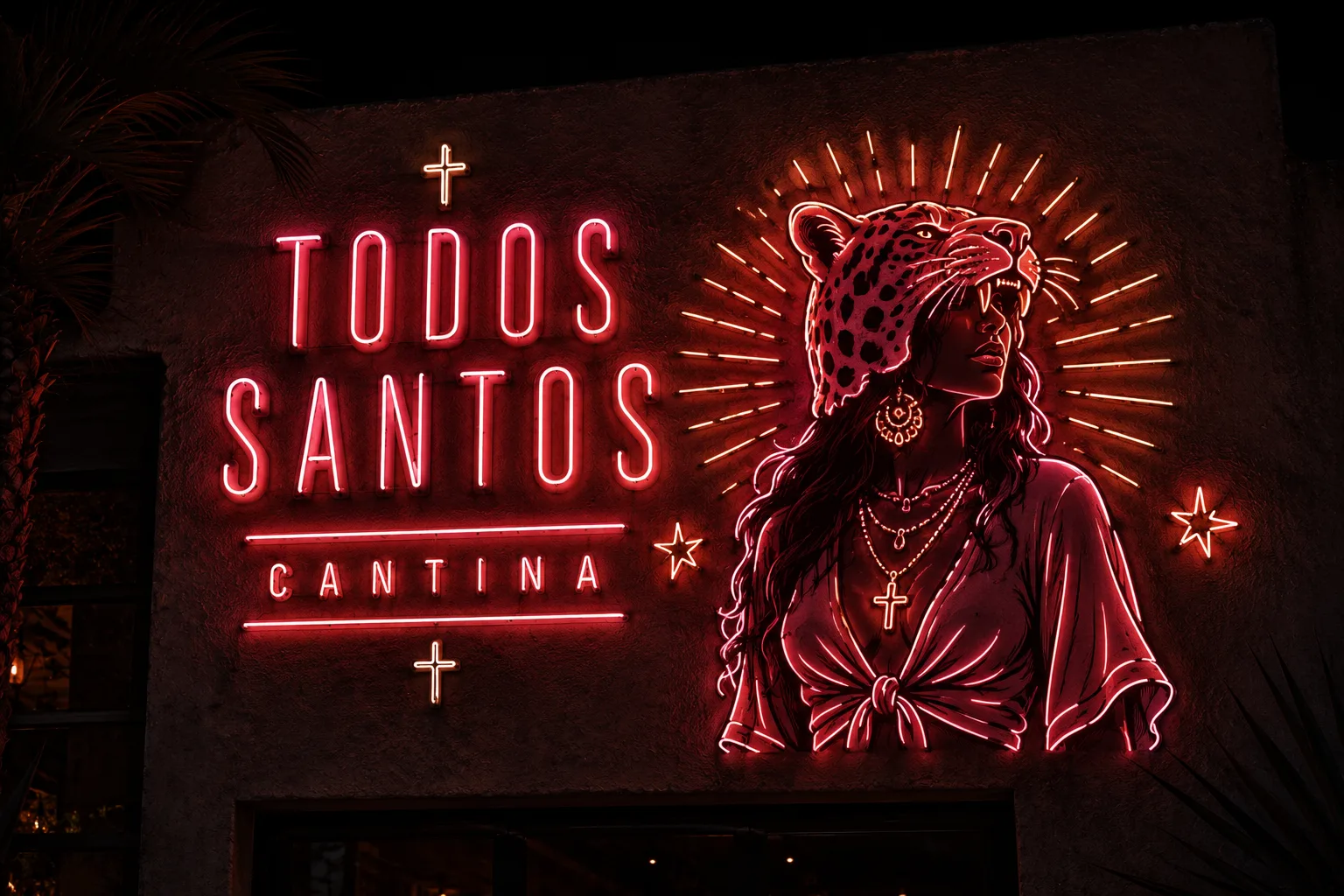 Todos Santos Cantina's neon facade at night: pink lettering beside a woman in a jaguar headdress framed by amber rays