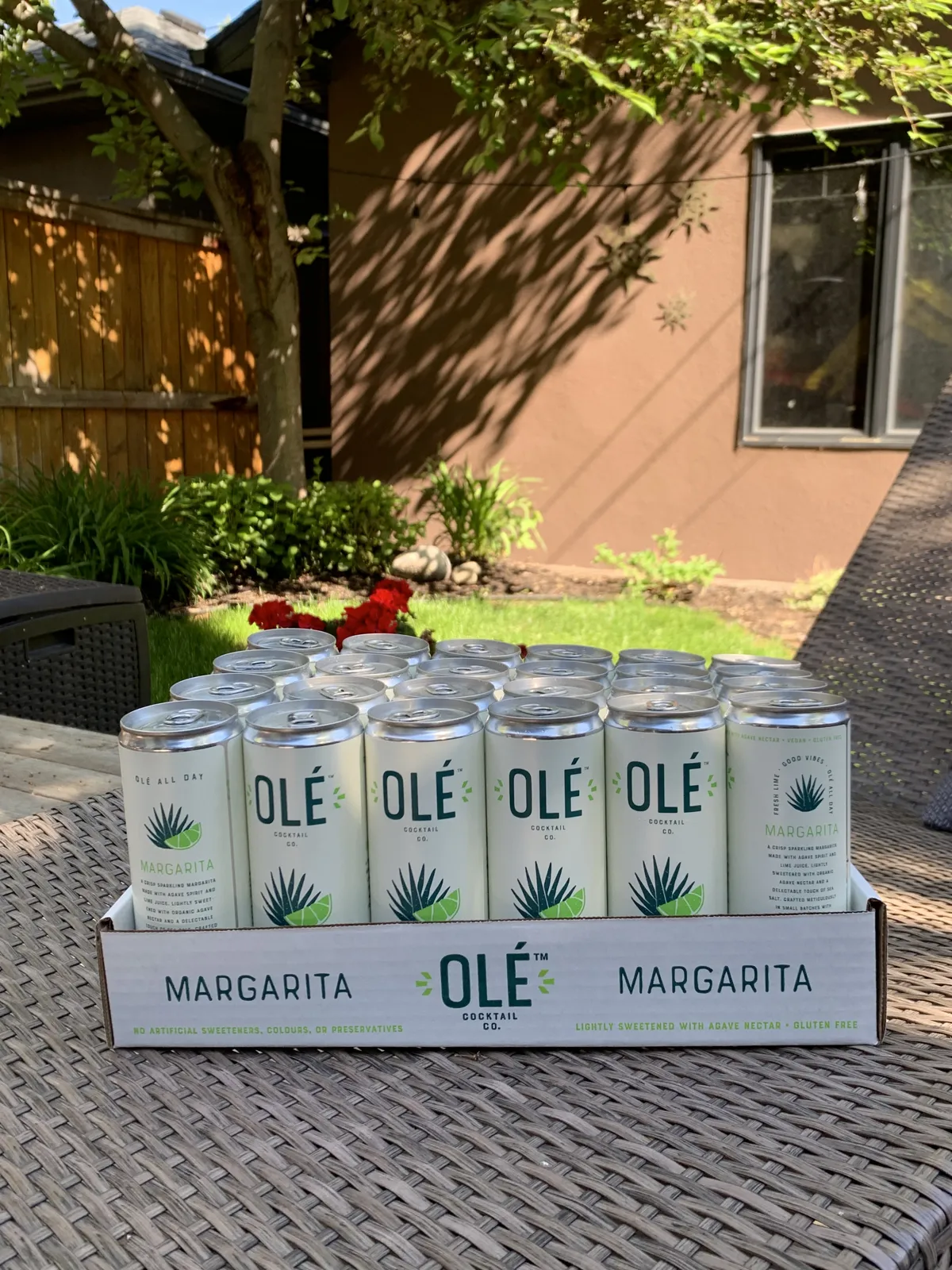 A case of Olé Cocktail Co margarita cans on a patio table in the sun
