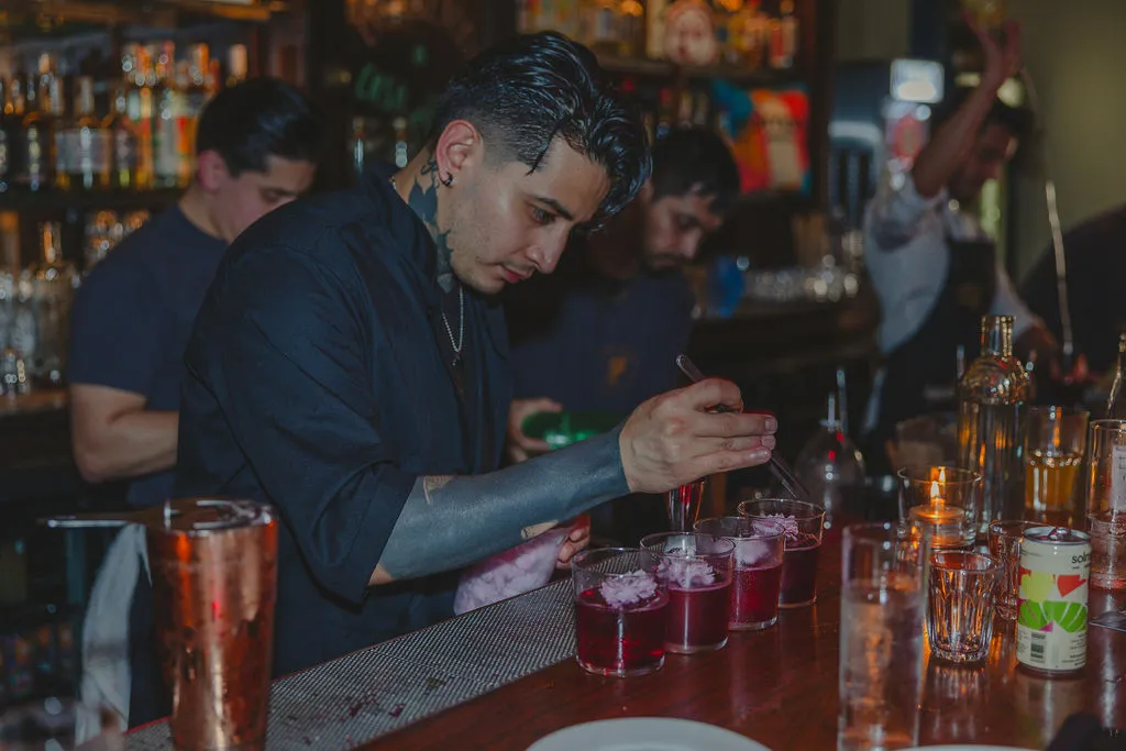 Bartenders build a round of cocktails on a busy bar, with a Solmano can on the counter
