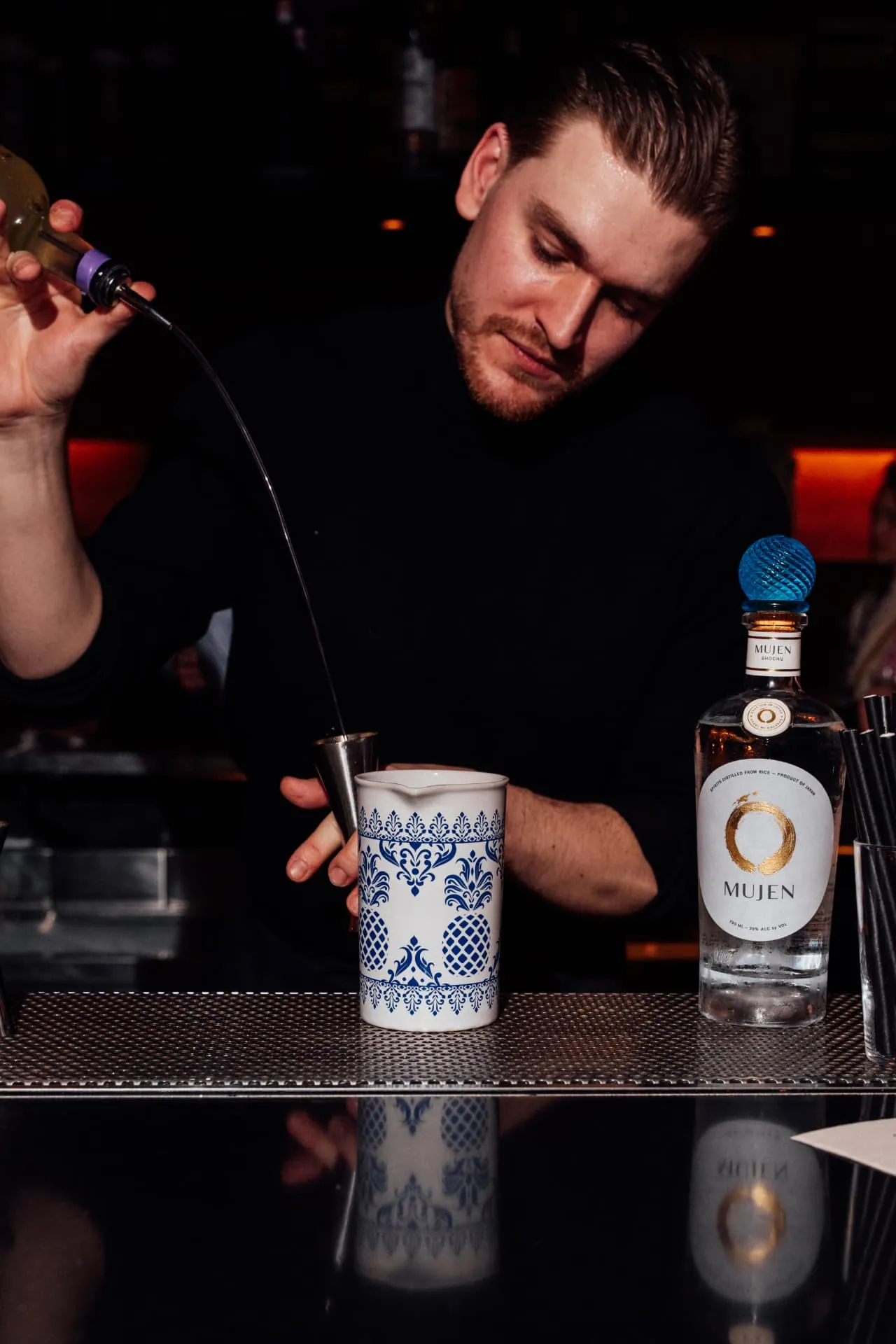 A bartender measures a pour beside a bottle of Mujen shochu at a 50 Best bar event